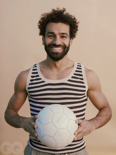 a man is holding a soccer ball in his hands and smiling at the camera while wearing a striped tank top