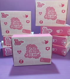 four boxes with different designs on them sitting on a purple surface in front of a pink background