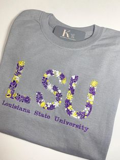 Custom University Embroidered Floral Tee. This unique shirt features delicate embroidered flowers on the letter initials of the college of your choice, adding a feminine touch to your fan gear. Gildan College Shirt Design Ideas, Embroidered Short Sleeve College T-shirt, College Embroidered Short Sleeve T-shirt, Embroidered Short Sleeve T-shirt For College, Casual T-shirt With Multicolor Letter Embroidery, Casual Multicolor Embroidered Letter T-shirt, College Shirts Design, College Shirt Diy, College Shirt Design