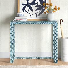 a blue and white console table with flowers in vase next to it on the floor