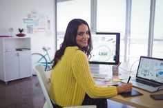 a woman sitting at a desk in front of a laptop computer with a monitor on it