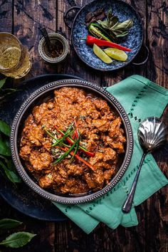 a bowl filled with meat sitting on top of a wooden table next to other dishes