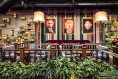 an indoor restaurant with two large paintings on the wall and potted plants in the foreground