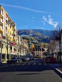 a city street with cars parked on both sides and mountains in the distance behind it