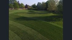 an aerial view of a green golf course with trees in the background and blue sky