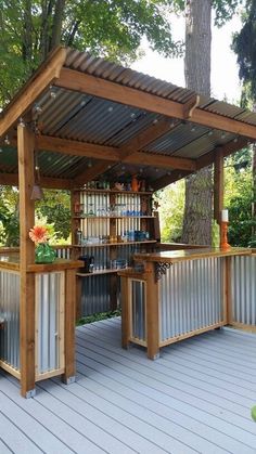 an outdoor bar made out of metal and wood with a roof over it, on a deck