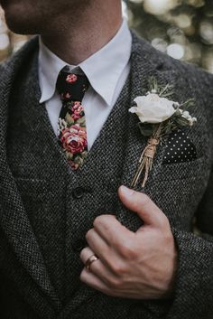 a man wearing a suit and flower boutonniere is holding his hand in his pocket