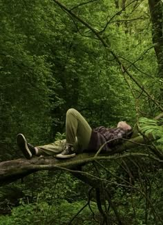 a man laying on top of a fallen tree in the forest with his head down