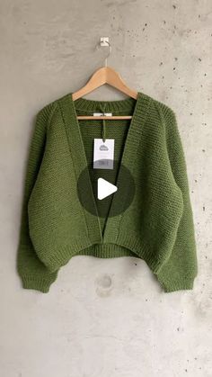 a green sweater hanging on a hanger next to a white wall with an arrow