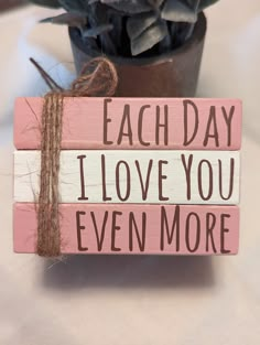 a wooden sign that says each day i love you even more next to a potted plant