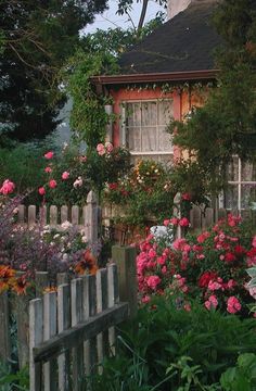 a garden with pink and white flowers in front of a house