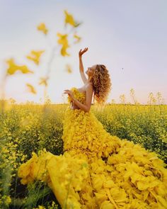 a woman in a yellow dress is standing in a field with her hands up to the sky