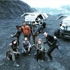 a group of people standing next to each other in front of some vehicles on a mountain