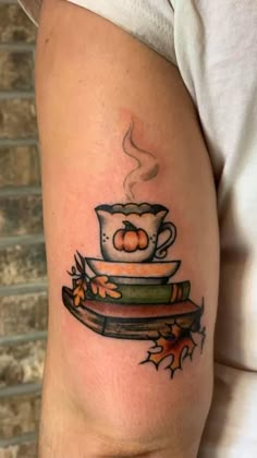 a person with a tattoo on their arm holding a coffee cup and stack of books