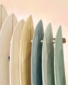 five surfboards are lined up in a row against a pink sky and sand background