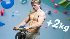 a man with no shirt is holding a barbell in front of a climbing wall