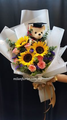 a bouquet of sunflowers and roses with a teddy bear wearing a graduation cap