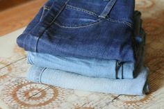 three pairs of blue jeans stacked on top of each other in front of a rug