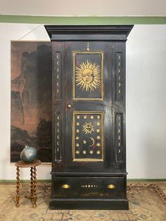 an antique armoire with sun and moon designs on the door, next to a small table