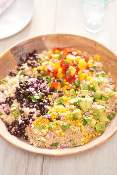 a wooden bowl filled with black beans, corn, and avocado on top of a white table