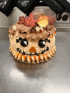 a cake decorated to look like a scarecrow with eyes and nose, sitting on top of a metal surface