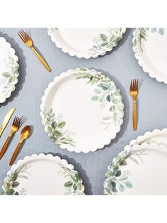 there are many plates with gold forks and knives on the tablecloth, which is decorated with green leaves