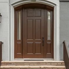 a brown front door and steps leading to a white house with two lights on each side