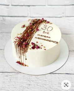 a white cake decorated with flowers and chocolate icing on a plate next to a brick wall