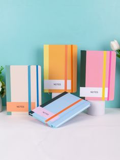 three notebooks are lined up next to each other on a table with flowers in the background