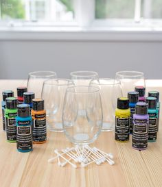 several wine glasses are sitting on a table with paint bottles and glues in front of them