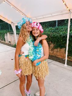 two girls in hula skirts are hugging each other under a tent with string lights