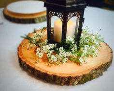 a lit candle sits on top of a piece of wood with flowers and greenery