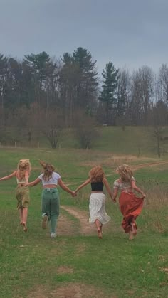 four girls are running down a path holding hands in the grass with trees in the background