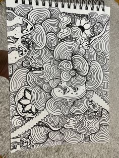 a spiral notebook with black and white doodles on the cover, next to a person's hand