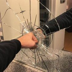 a hand holding a broken glass in the middle of a counter top with another hand reaching for it