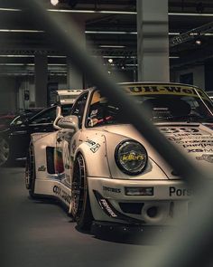 two porsches are parked in a garage with other cars behind the fenced off area