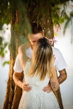 a man and woman standing next to each other under a tree with their arms around each other