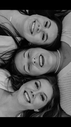 three women are laying down on the ground smiling at the camera, with their heads together