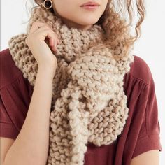 a woman is wearing a knitted scarf in beige and brown colors, she has her hands on her shoulder