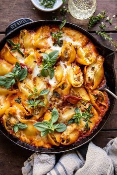 a skillet filled with pasta and sauce on top of a wooden table next to a towel