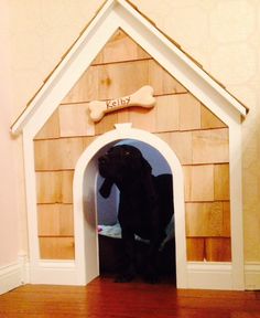 a dog house with a large black dog in it's doorway and a bone on the wall