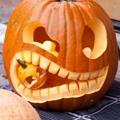 a carved pumpkin sitting on top of a table next to another pumpkin with it's mouth open