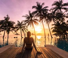 a woman sitting on top of a wooden dock next to a swimming pool at sunset