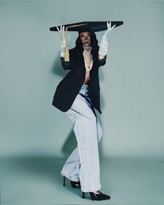 a woman with a hat on her head is posing in jeans and heels while holding a skateboard over her head