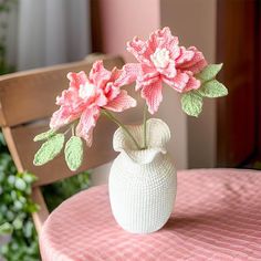 a white vase filled with pink flowers sitting on top of a table next to a wooden chair