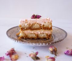 a piece of cake sitting on top of a glass plate next to dried pink flowers