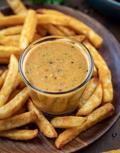 a wooden plate topped with french fries next to a bowl of dipping sauce on top of it