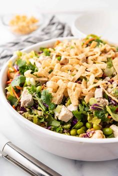 a white bowl filled with salad on top of a table next to silver utensils