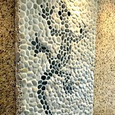 an artistic tile design on the side of a wall in a public restroom, with black and white pebbles embedded in it