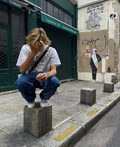 a woman sitting on top of a cement block while talking on a cell phone in front of a building